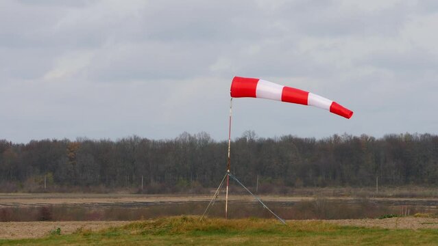 Moving air sleeve windsock show direction of wind blowing near aircraft landing place site on background of trees. Static shot.