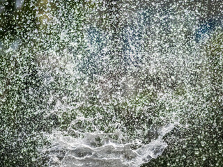 Splashes of water on dark background. Water sprays in sunny day close-up.