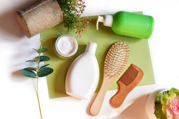 Toiletries kit, natural bath products flat lay photography. White shampoo bottle, facial cream, wooden hair brushes, liquid soap and plants on a green background