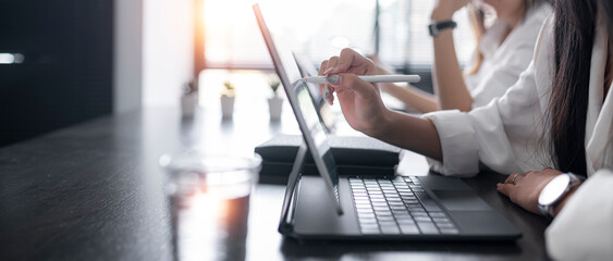 Young woman using stylus pen writing on tablet screen, working together at office.