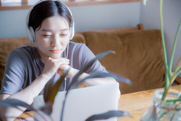 明るい植物のある窓辺の部屋でノートパソコンでオンライン授業,リモートワークをする日本人女性