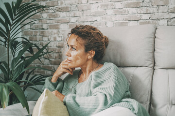 Thoughtful and worried lady at home sitting on the sofa looking serious and thinking a lot. Female portrait indoor. Lady sit on the couch touching his face with problems in mind. Finding ideas concept
