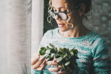 Close up portrait of young mature woman having care of a green plant at home in indoor leisure...