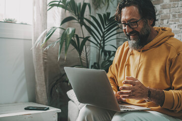 Mature man working on laptop at home sitting on the sofa. Modern technology leisure indoor activity. Online people busy on video call with computer and internet connection. Happy worker in free office