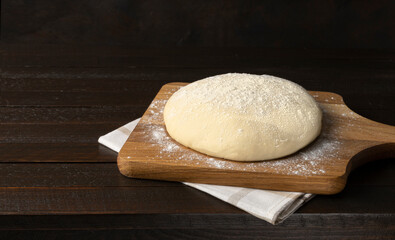 Fresh yeast dough isolated on wooden cutting board on dark background.
