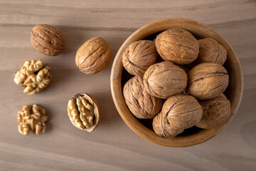 Bowl of walnuts and whole walnut kernels on wooden background,top view