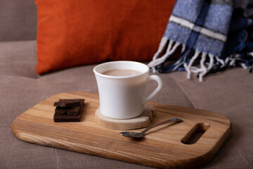 Autumn mood composition with cup of cocoa and chocolate, plaid and books on sofa background. Hot drink in autumn concept