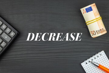 DECREASE - word (text) and euro money on a wooden background, calculator, pen and notepad. Business concept (copy space).