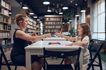 Fototapeta premium Teacher playing with schoolgirl rock, paper, scissors game in afterschool club. Child playing in school library after classes at primary school. Back to school