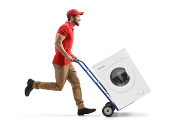 Full length profile shot of a male worker running and pushing a hand-truck with a washing machine - obrazy, fototapety, plakaty