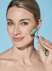 Face jade roller. Face of beautiful woman with green jade roller for anti-aging procedures