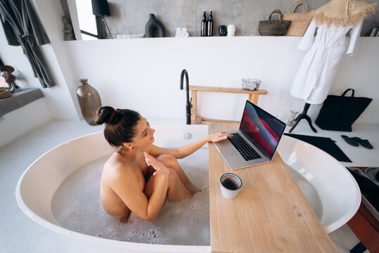 Young woman working on laptop while taking a bathtub