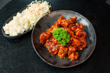 Korean Fried Chicken Sweet Spicy Gangjung, traditional Korean confectionery crackers coating with a syrup on grill plate with pickle dishes on black table background
