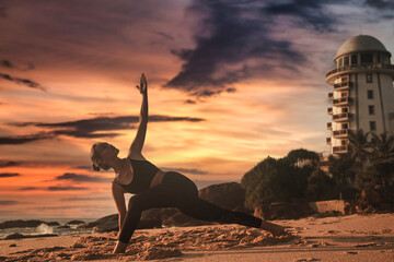 Young woman does yoga for healthy lifestyle on tropical sea or ocean beach outdoors on sunset