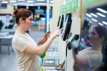 A frustrated woman uses a self-checkout counter. The girl does not understand how to independently buy groceries in the supermarket without a seller