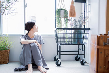 明るい植物のある窓辺の部屋で座って空を見上げて休憩する日本人女性