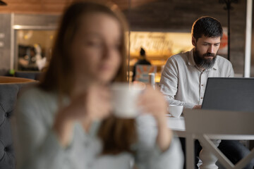 successful business man sitting at the cafe working on a laptop, girl is blurred on foreground, work of freelancer