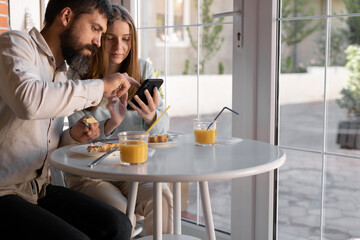 Young couple at cafe, she is drinking juice, he is showing her something in his mobile phone. They are happy