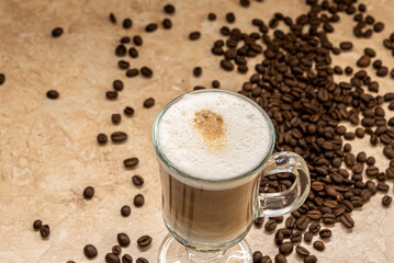 A glass cup of cappuccino coffee on the table and coffee beans.