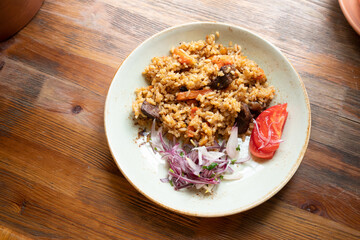 Pilaf with rice and beef or lamb, tomato and marinated red onion on plate on wooden table. Lifestyle, selective focus, top view, flat lay.