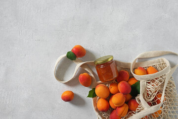 apricots in string bag and jar with apricot jam on white table. copy space. top view