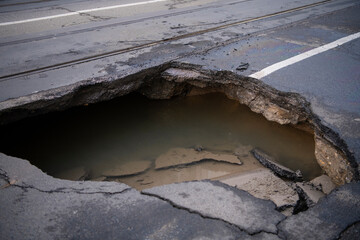 Huge sinkhole on busy asphalt road surface on which cars drive. Accident situation on a city street...