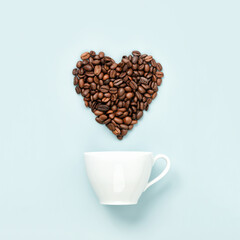White coffee cup and coffee beans in shape of heart on blue background, flat lay