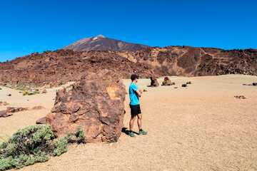 Rear view of hiking man with scenic view on moon landscape of Minas de San Jose Sur near volcano Pico del Teide, Mount El Teide National Park, Tenerife, Canary Islands, Spain, Europe. Lava rocks