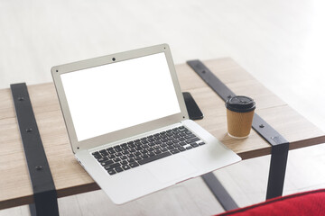 Mockup laptop computer with blank white screen on small table with coffee paper cup.