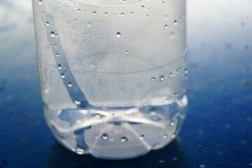 Leere Wasserflasche mit Wassertropfen auf blauem Metalltisch bei Sonne am Morgen im Sommer