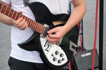 Straßenmusiker in weißem T-Shirt spielt auf schwarzer E-Gitarre 
