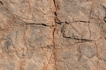 Stone wall is sandy in color with deep cracks and various bulges. Stone textured background of sand color with cracks.