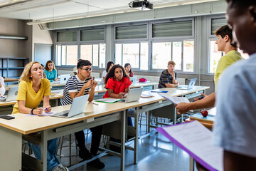 Young group of diverse high school students giving a presentation to classmate friends in classroom - Male and female college student attending to classmates lecture - Diversity and education concept - obrazy, fototapety, plakaty
