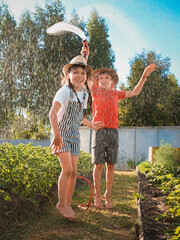 Sibling children frolic splashing with a water hose in the backyard in the garden on summer...