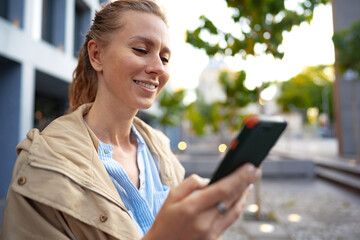 Handsome young smiling woman with mobile phone walking on the street