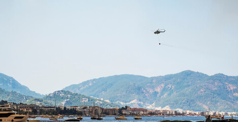 Helicopter going to fire area to extinguish forest fire. Helicopter with a water bucket on a blue...