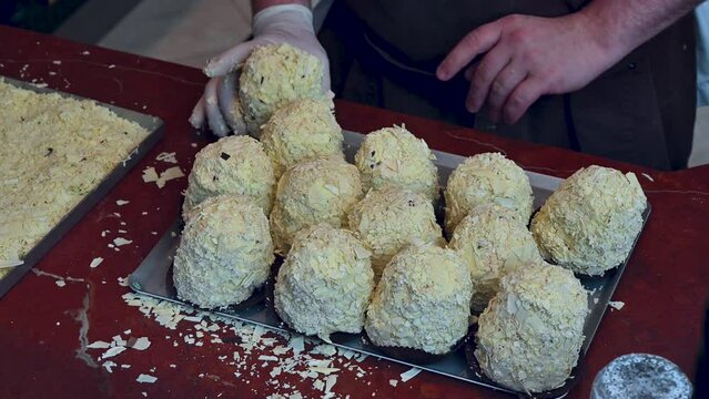 Paris, France, June 2022. Footage of a pastry chef in a shop window preparing sweets by rolling them one at a time on a tray sprinkled with chopped almonds and hazelnuts.