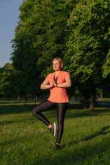 Middle aged caucasian woman doing balance yoga asana in park on summer sunset day 