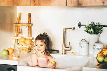 Funny happy baby girl playing in a kitchen sink.