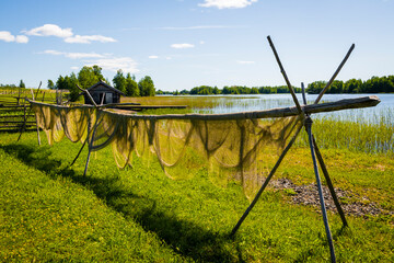 A summer rural landscape, hanging drying fishing nets in the fresh air on the shore of the lake. - obrazy, fototapety, plakaty