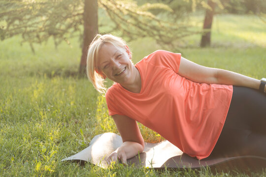 Happy smiling middle aged woman portrait in park. Laying woman on sport mat after workout 