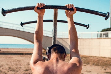 Back view of a young caucasian boy tired and holding from a pull up bar. Calisthenics training.