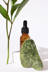 Cosmetic bottle with dropper on podium, jade Gua sha stone for face massage. Serum container and...
