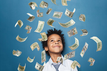 Successful little black kid boy standing under us dollar money rain on blue background
