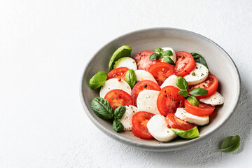 Caprese salad with tomatoes mozzarella basil and olive oil with a basil leaf near on white background. Text space