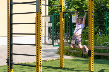 Caucasian girl 6 years old, goes in for sports, pulling up on the horizontal bar, summer on the sports ground.