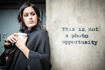 A Photo Opportunity. A beautiful young mixed race girl posing ironically by a graffiti slogan. From a series of images with the same model.