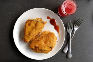 Rustic homemade Bread Pakora or triangle shape pakoda served with tomato ketchup on a brekfast table along with watermelon juice, fruits and tea. Indian tea-time snack. Copy space
