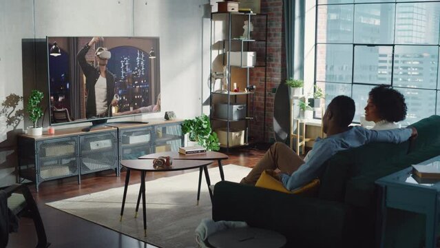 Lovely Happy Black Couple Watching Television in the Stylish Living Room. Girlfriend and Boyfriend Enjoy Sitcom on Streaming Service Sitting on Couch.