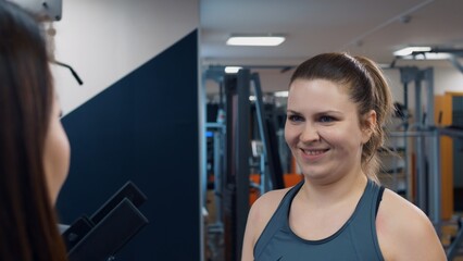 Women in the gym talk about abstract topics and laugh. The gym is not only a place for training but also for communication with friends and a coach. Gym life for women who take care of their body.